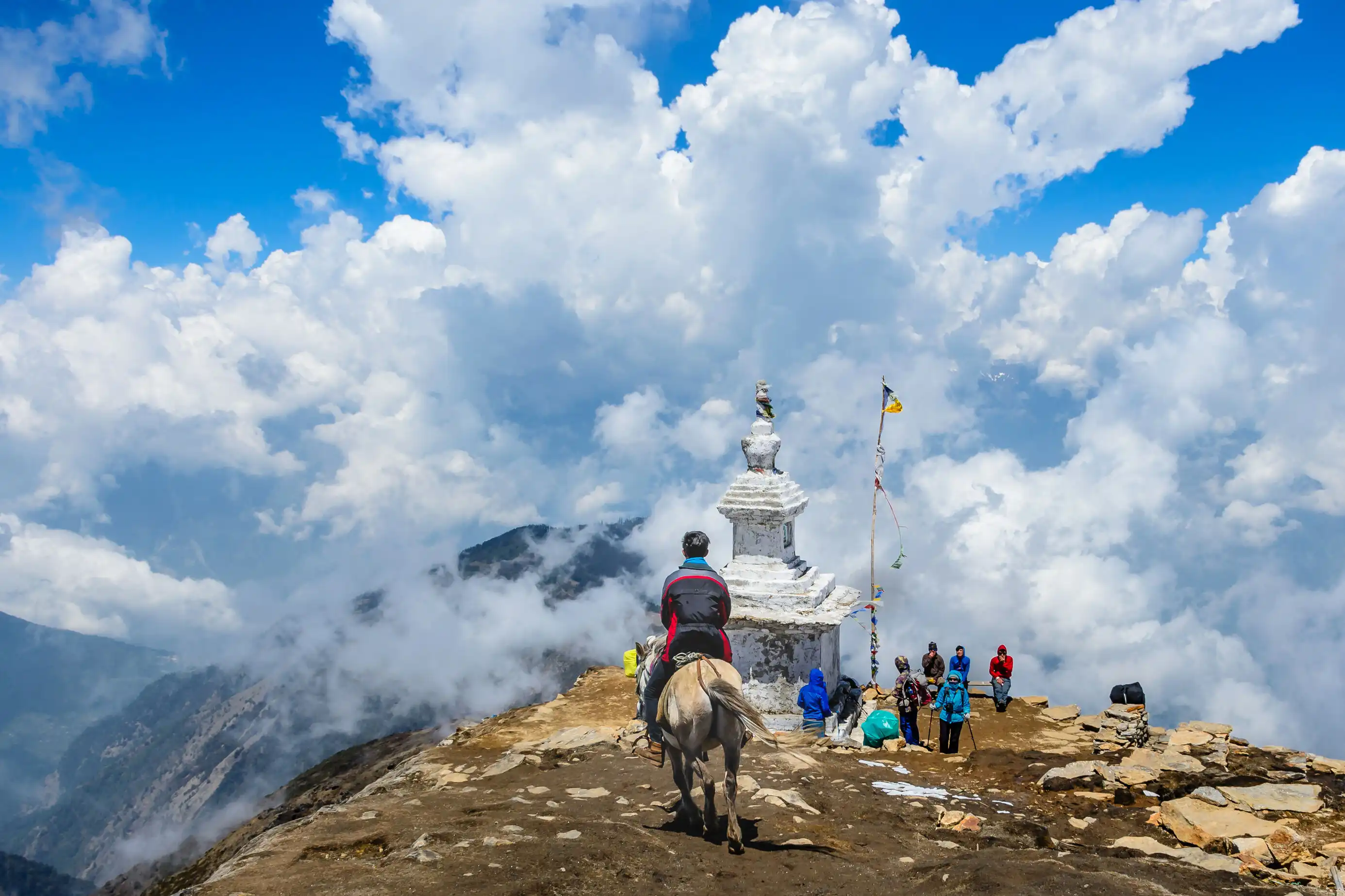 Person on horseback and hikers near a white stupa on a cloudy mountain ridge in Helambu.