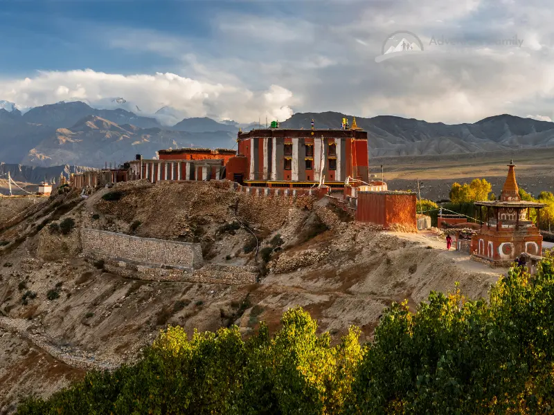 Four hikers ascending green mountain with cliffs and snow-capped peak in Upper Mustang.