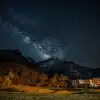 Milky Way stretching across a starry night sky above mountains, with a brightly lit building at the base.