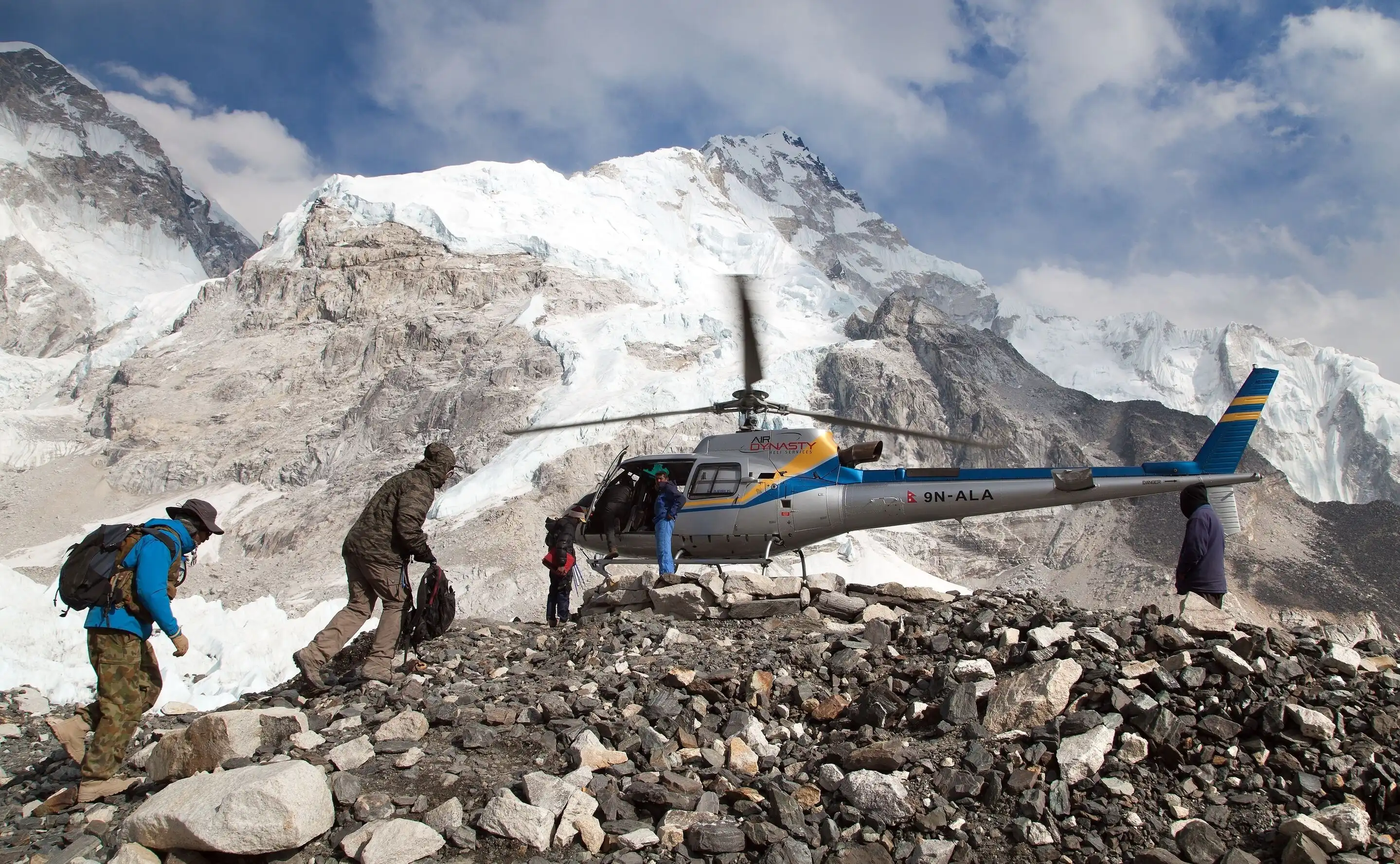 Helicopter on rocky snowy mountain with people in outdoor gear approaching (Everest Base Camp Heli Tour).