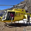Yellow helicopter on snowy Everest terrain with people in pink jackets.