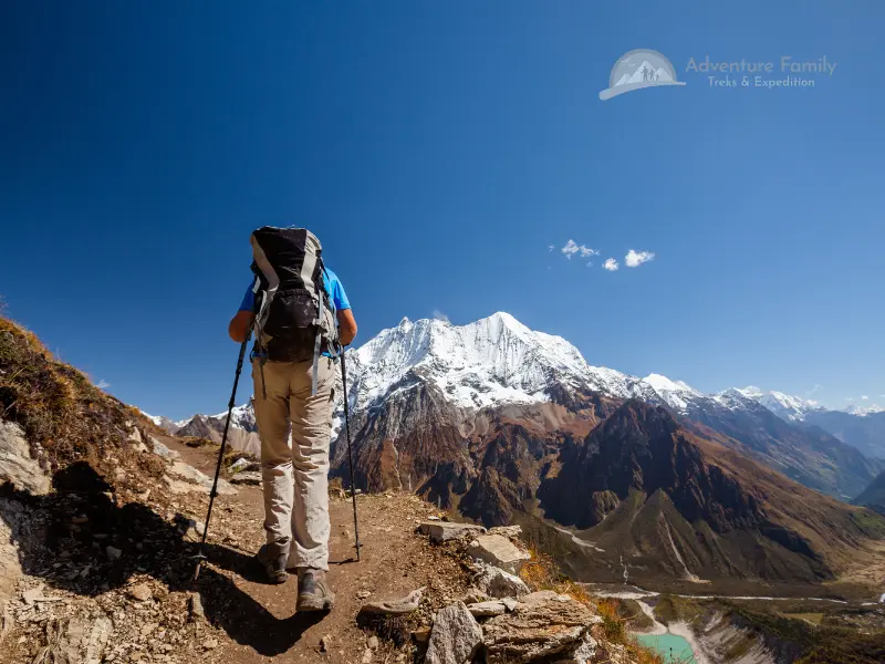 Hikers with backpacks on trail with snow-capped Manaslu mountains in background.