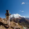 Hikers with backpacks on trail with snow-capped Manaslu mountains in background.