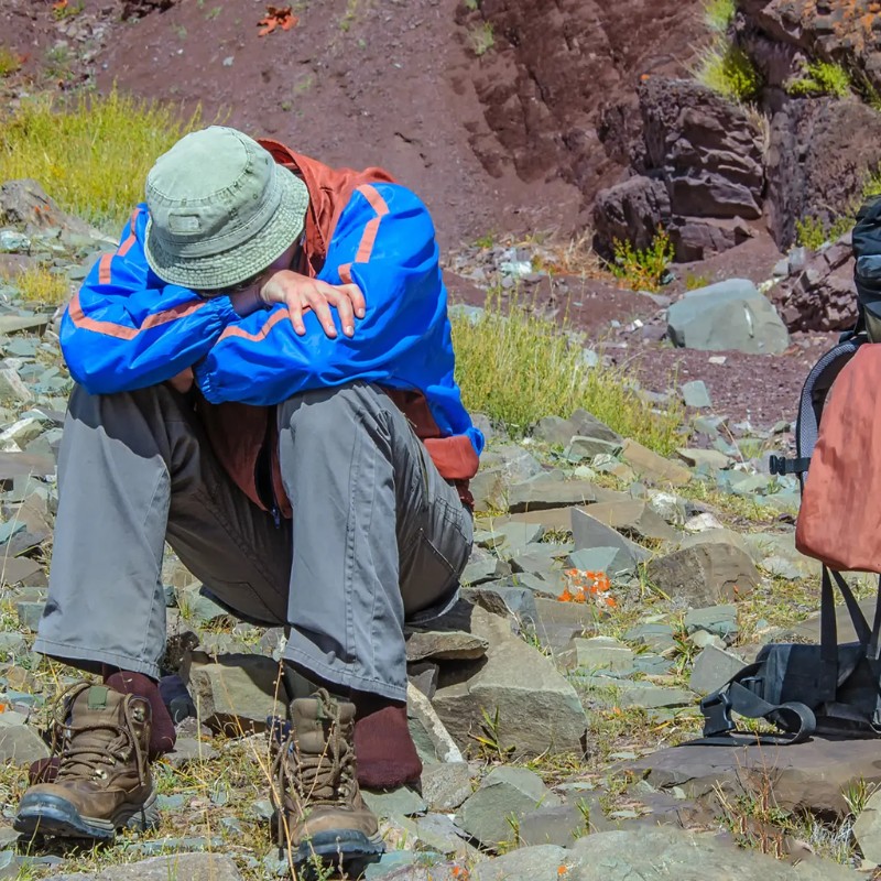 Trekker resting on rocky ground while experiencing altitude sickness in the mountains