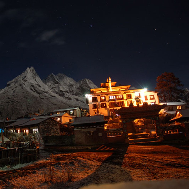 Tengboche Monastery illuminated at night beneath snowy Himalayan peaks and a starry sky