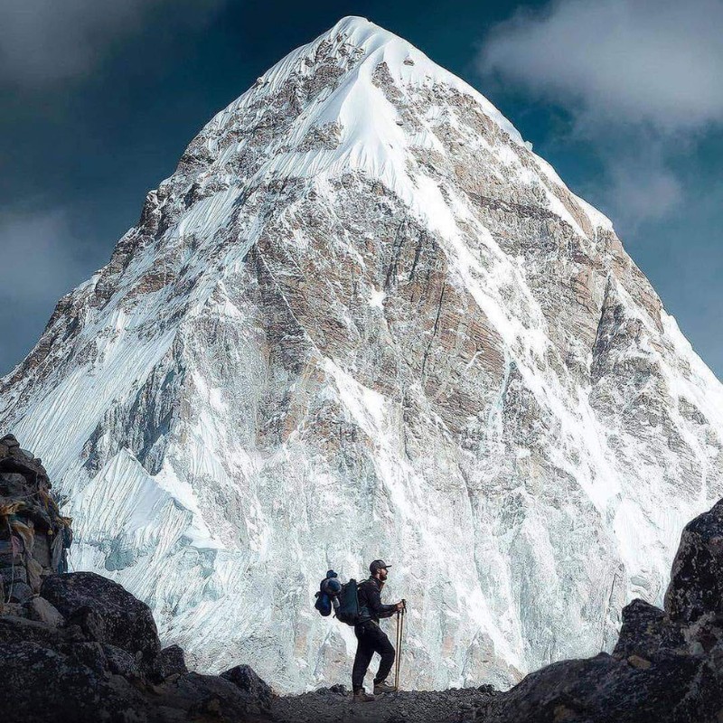 Photographer silhouetted on a rocky ridge at Kala Patthar with Mount Pumori towering in the background, showcasing the dramatic snow-covered Himalayan peak in Nepal.