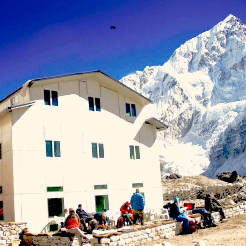 Lodge in Gorakshep with trekkers resting beneath snowy Himalayan peaks near Everest Base Camp.