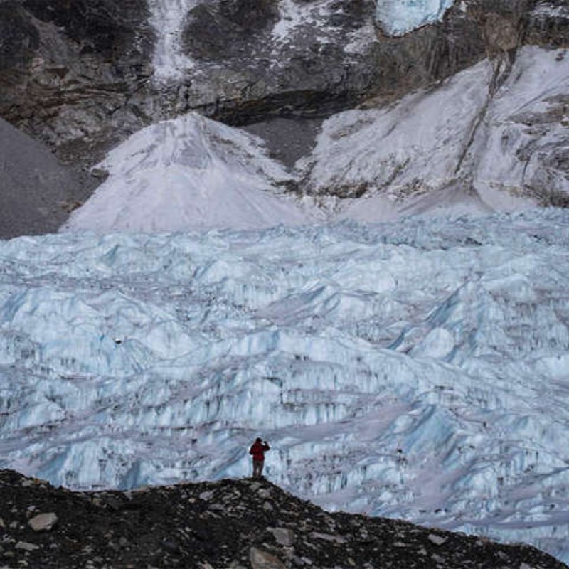 Massive icy Khumbu Glacier near Lobuche with a lone trekker standing on rocky terrain.