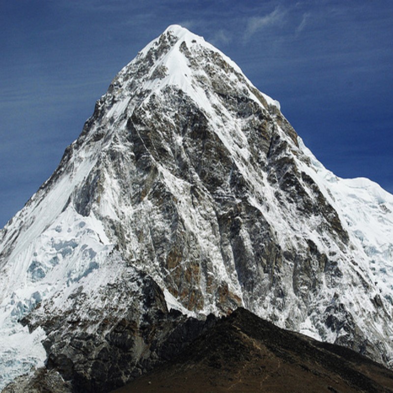 Mount Pumori covered in snow and ice, rising sharply above the Himalayan landscape near Everest in Nepal, with rugged rock faces and a clear blue sky background.