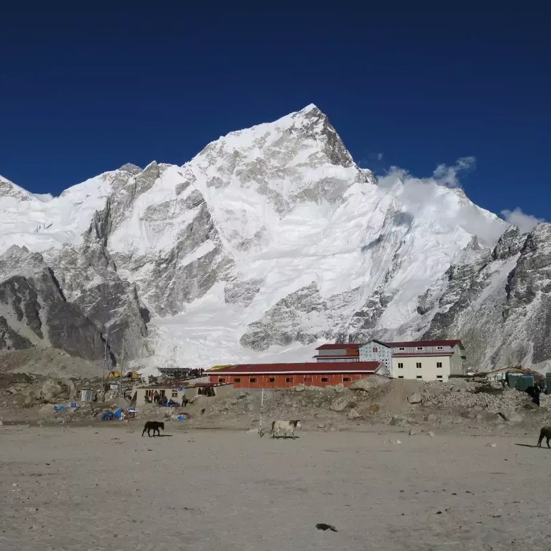 Mount Nuptse towering above Everest Base Camp in Nepal, with snow-covered Himalayan peaks, rugged glacier terrain, and trekking lodges under a clear blue sky.