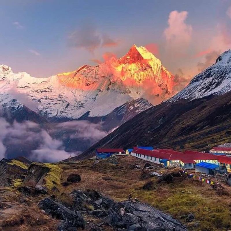 Snow-covered Himalayan mountain peak glowing at sunrise above a high-altitude trekking lodge in Nepal