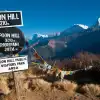 Colorful prayer flags and signs at Poon Hill with snow-capped mountains and clear sky.